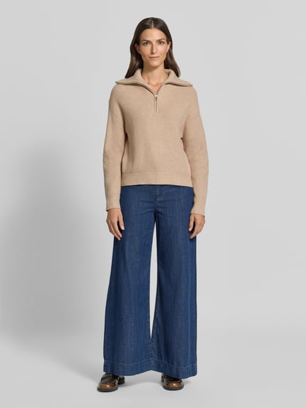 Frauenmodel trägt Troyer aus Viskose-Mix mit gerippten Abschlüssen Modell 'RIZON' von MANGO in Beige, kombiniert mit blauen Jeans, Ganzkörperansicht von vorne. Regular Fit, Troyer-Kragen, Rückenlänge 50 cm, Ärmellänge 52 cm.