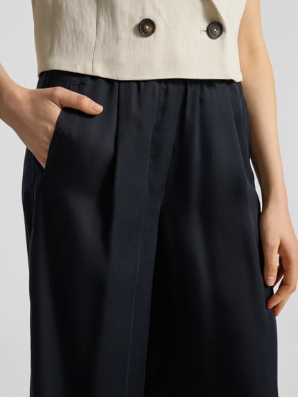 Frauenmodel trägt Wide Leg Stoffhose mit elastischem Bund von Lanius, reine Lyocell, schwarze Farbe, Eingrifftaschen, Nahaufnahme Oberkörper.