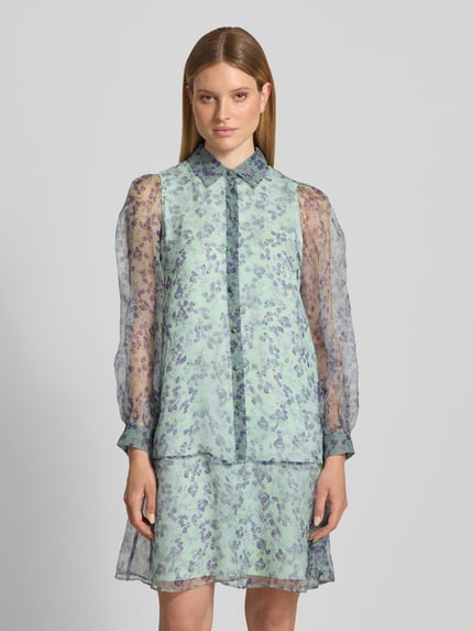 Kobiece modelka nosi Knielanges Kleid aus Seide mit Knopfleiste von Marc Cain, wzór na całej powierzchni, półprzezroczysty jedwab, prosty krój, długość do kolan, kołnierzyk koszulowy, listwa guzikowa, długość tyłu w rozmiarze 36: 94 cm, szerokość w rozmiarze 36: 50 cm, długość rękawów w rozmiarze 36: 64 cm. Ganzkörperansicht von vorne.
