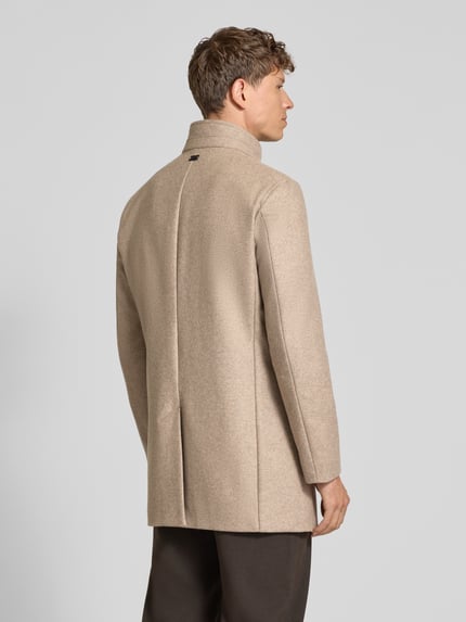 Männermodel trägt Mantel mit Stehkragen Modell 'Finlay 2.0' von Strellson in unifarbenem Beige mit Strukturmuster, Ganzkörperansicht Rückansicht.
