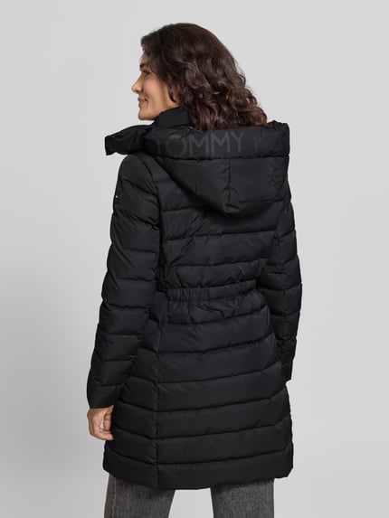 Frauenmodel trägt Daunenmantel mit Kapuze von Tommy Hilfiger, schwarz, Logo-Detail, metallische Akzente, Ganzkörperansicht Rückansicht