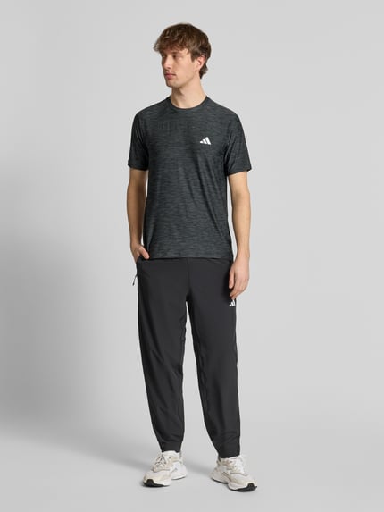 Männermodel trägt T-Shirt mit Label-Print von adidas Training in Dunkelgrau, sportlicher Material-Mix, Regular Fit, Ganzkörperansicht von vorne.