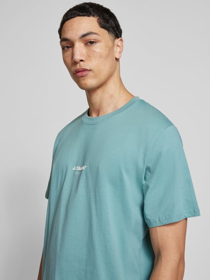 Mannenmodel draagt T-Shirt met Logo en Rundhalsausschnitt van Jack & Jones in turquoise, regular fit, bio-katoen, logo op borst, close-up bovenlichaam.