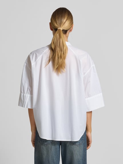 Frauenmodel trägt Boxy Fit Bluse mit Stehkragen und 3/4-Arm von Emily Van den Bergh aus reiner Baumwolle, Ganzkörperansicht Rückansicht.