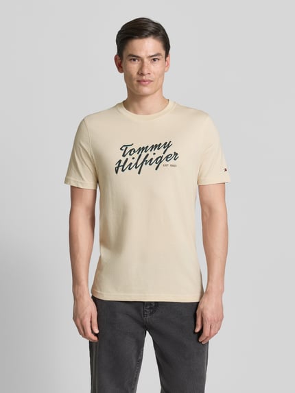 Mannelijk model draagt Regular Fit T-Shirt aus reiner Baumwolle van Tommy Hilfiger in effen beige, label print, ronde hals, korte mouw, jersey van puur katoen, vooraanzicht volledige lichaamsopname.