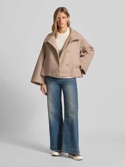 Frauenmodel trägt Jacke mit Stehkragen und Kimonoärmeln von Gina Tricot in Beige, Knopfleiste, gerader Schnitt, Ganzkörperansicht von vorne.