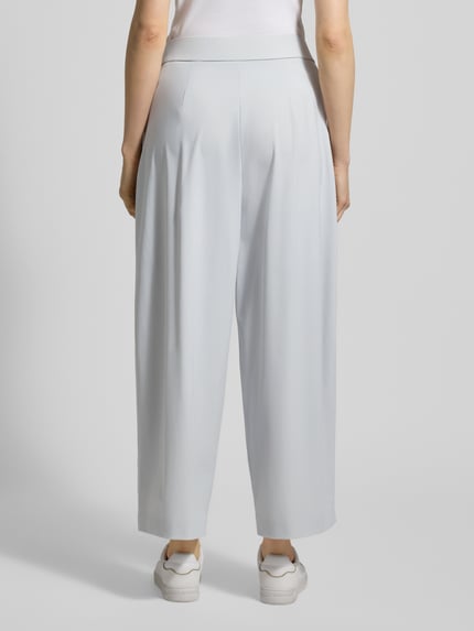 Frauenmodel trägt Hose mit gelegten Falten Modell 'MAYLA 6/8 JOGG' von Raffaello Rossi, hellgrau, elastischer Bund, weites Bein, Ganzkörperansicht Rückansicht.