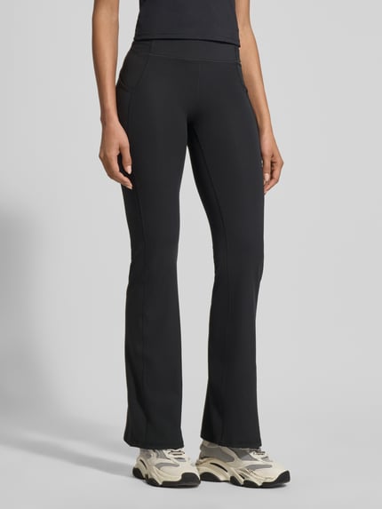Frauenmodel trägt Flared Fit Leggins mit Logo-Print Modell 'OASIS' von Fabletics in Schwarz, elastischer Bund, glatte Textur, Ganzkörperansicht von vorne.