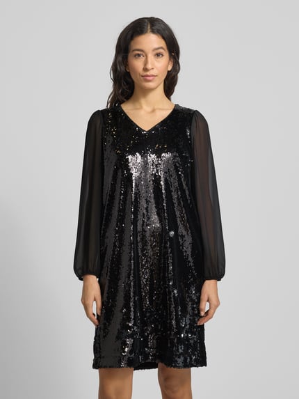 Kobiece model nosi Knielanges Kleid mit Paillettenbesatz von More & More, czarny kolor, elastyczna mieszanka materiałów, taliowany krój, długość do kolan, dekolt w serek, wycięcie w kształcie łezki na plecach, zapięcie na guzik, półprzezroczyste bufiaste rękawy, cekinowe obszycie, długość tyłu 92 cm, szerokość klatki piersiowej 50 cm, długość rękawa 60 cm, widok z przodu całej sylwetki.