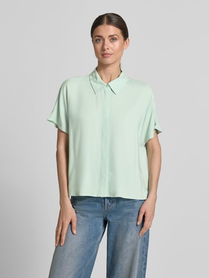 Frauenmodel trägt Relaxed Fit Kurzarmbluse aus Viskose von Tom Tailor Denim, unifarben, einreihige Knopfleiste, Hemdblusenkragen, Ganzkörperansicht von vorne.