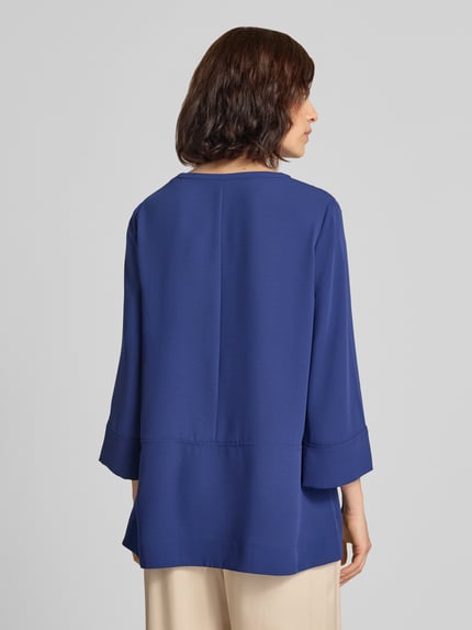 Frauenmodel trägt Regular Fit Bluse mit V-Ausschnitt und 3/4-Arm von Marc Cain in Blau, Teilungsnähte, Rückansicht, Ganzkörperansicht.