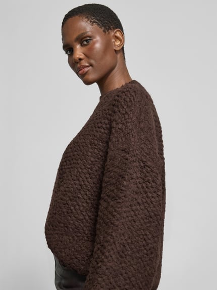 Frauenmodel trägt Pullover mit asymmetrischem Saum Modell 'CORSETTA' von black palms, unifarben, strukturierte Strickoptik, Langarm, Nahaufnahme Oberkörper.