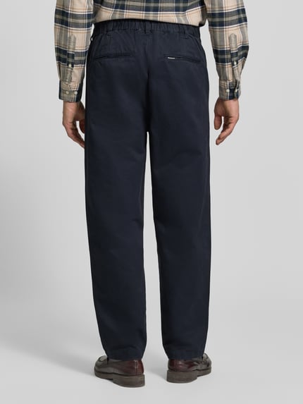 Männermodel trägt Bundfaltenhose mit Twillstruktur von Barbour in Dunkelblau, unifarben, Gesäßtaschen, Bundfalte, Ganzkörperansicht Rückansicht.