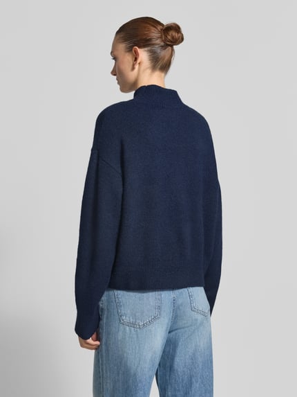 Młody modelka nosi sweter z dzianiny 'Turtleneck-Pullover mit Woll-Anteil und Rundhalsausschnitt' od Neo Noir, Mieszanka materiałów z dodatkiem wełny, prosty krój, prążkowane wykończenia, prążkowany okrągły dekolt, długie rękawy, długość tyłu 53 cm w rozmiarze 36, Długość rękawów 53 cm w rozmiarze 36, widok całej sylwetki z tyłu.