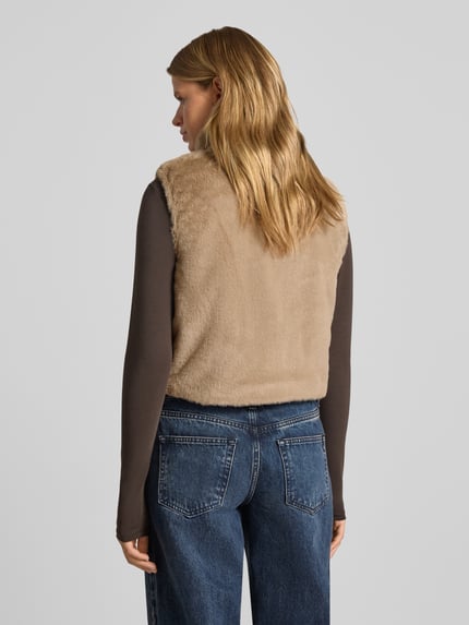 Vrouwenmodel draagt Regular fit bodywarmer met wendfunctie model 'DANA' van ONLY in beige, zachte textuur, dames bodywarmer, totale achteraanzicht.