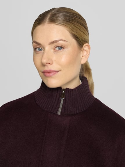 Frauenmodel trägt Mantel aus Woll-Mix mit gestricktem Stehkragen von COMMA in dunklem Lila, sichtbare Struktur, Nahaufnahme Oberkörper. Kontext: Damen Mantel, Woll-Mix mit Viskose-Anteil, Straight Fit, Reiß- und Druckknopfverschluss, seitliche Eingrifftaschen, gestrickte Ärmelabschlüsse, Rückenlänge 92 cm, Schulterbreite 40 cm, Brustweite 60 cm, Ärmellänge 63 cm.
