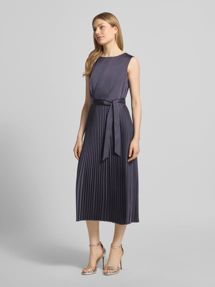 Modelka nosi Midikleid mit Plisseefalten und Bindegürtel von comma, ciemnoszary materiał z domieszką stretchu, linia A, plisy, pasek, Szerokość w rozmiarze 36: 40 cm, długość tyłu 35 cm, zdjęcie całej sylwetki z przodu.