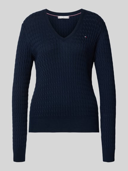 Vrouwenmodel draagt Regular Fit Strickpullover aus reiner Baumwolle van Tommy Hilfiger, donkerblauw, kabelpatroon, logo detail, V-hals, lange mouwen, geribde boorden, gebreide katoen, unikleuren. Ganzkörperansicht van voren.