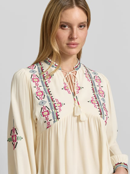 Frauenmodel trägt Tunikabluse mit Motiv-Stitching Modell 'TILT' von Bash in Creme mit bunten Stickereien aus reiner Viskose, Nahaufnahme Oberkörper.