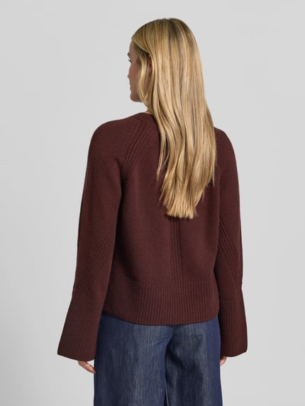 Frauenmodel trägt Pullover mit ausgestelltem Ärmel Modell 'Maple' von Joseph in unifarbener Strickoptik, strukturierte Feinstrick-Oberfläche, Regular Fit, cropped Länge, Rundhals, lange Raglanärmel, gerippter Rumpfabschluss, dunkles Braun, Ganzkörperansicht Rückansicht.
