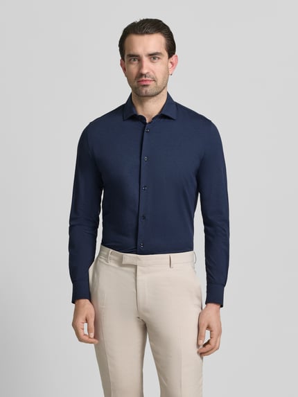 Männermodel trägt Slim Fit Business-Hemd mit Knopfleiste von CRUNA in Dunkelblau, Material-Mix mit Stretch, Kentkragen, Ganzkörperansicht von vorne.