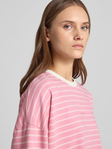 Vrouwenmodel draagt Regular Fit Longsleeve uit puur katoen van OH APRIL in roze met witte strepen, ronde hals, detailopname zijkant, ruglengte bij maat S 53 cm.