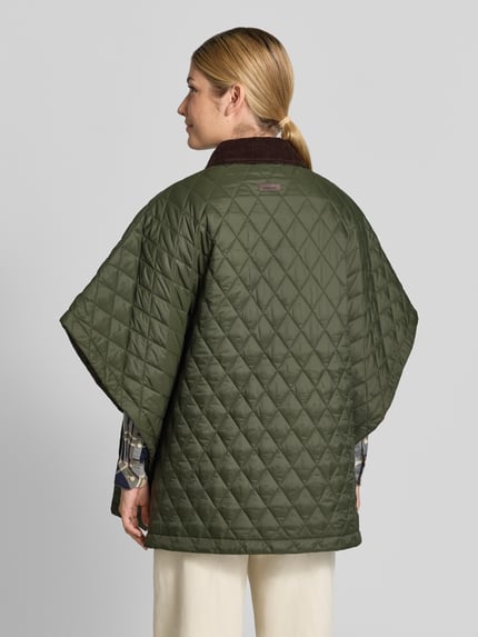Frauenmodel trägt Oversized Poncho mit Umlegekragen Modell 'MILDRED QUILTED CAPE' von Barbour in Olivgrün mit Rautensteppung, Damen Poncho von Barbour, Ganzkörperansicht Rückansicht.