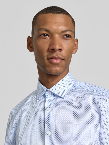 Männermodel trägt Regular Fit Businesshemd mit Kentkragen von OLYMP, Popeline mit geometrischem Allover-Muster, Nahaufnahme Oberkörper.