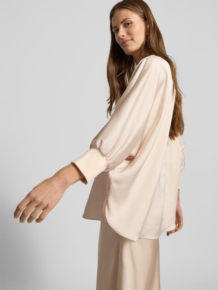 Frauenmodel trägt Blusenshirt aus Satin mit 3/4-Arm von JOOP!, Relaxed-Fit, Rundhalsausschnitt, beige, glatte Struktur, Ganzkörperansicht Rückansicht.