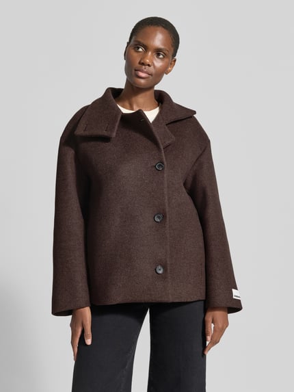 Frauenmodel trägt dunkelbraunen Loose Fit Kurzmantel aus Wolle Modell 'MAJELAA WOOL' von ARMEDANGELS, Filz-Textur, Ganzkörperansicht von vorne.