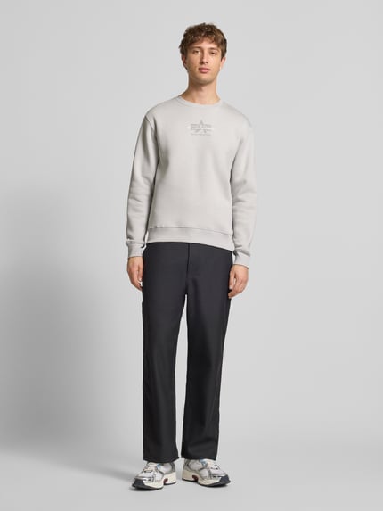 Männermodel trägt Regular Fit Sweatshirt aus Baumwoll-Mix mit Label-Detail von Alpha Industries in Hellgrau, elastische Abschlüsse, Ganzkörperansicht von vorne. Rückenlänge bei Größe M: 66 cm.