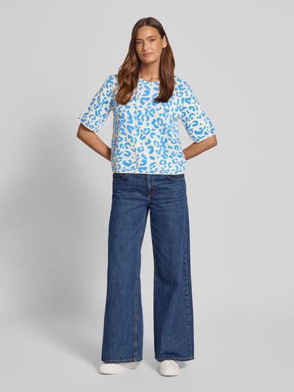 Modelka nosi koszulkę Relaxed Fit Shirt aus Viskose-Anteil Modell 'Mayas' od Vila, mieszanka materiałów z dodatkiem wiskozy, imitacja dzianiny, rękaw o dł. 1/2, zwierzęcy nadruk na całej powierzchni, okrągły dekolt, długość tyłu w rozmiarze S: 54 cm, długość rękawów w rozmiarze S: 29 cm, widok całej sylwetki z przodu.