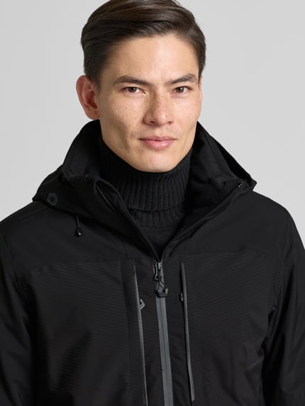 Männermodel trägt Jacke mit Kapuze von Icepeak in Schwarz, Material-Mix, Regular-Fit, Reißverschluss, Reißverschlusstaschen, Nahaufnahme Oberkörper. Rückenlänge 77 cm, Schulterbreite 47 cm, Brustweite 58 cm, Ärmellänge 72 cm bei Größe 50.