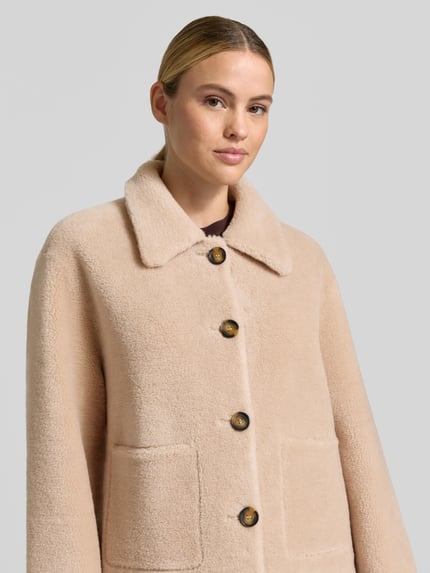 Frauenmodel trägt Regular Fit Jacke aus reiner Wolle von OAKWOOD in Beige mit Umlegekragen und großen Knöpfen, Nahaufnahme Oberkörper.