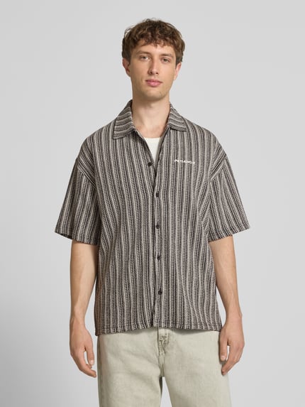 Męski model nosi Relaxed Fit Freizeithemd mit Label-Stitching Modell 'Forno' od Pegador z bawełny, cały wzór, kołnierzyk kent, beżowo-czarne kolory, długość tyłu w rozmiarze M: 74 cm, szerokość ramion w rozmiarze M: 40 cm, długość rękawa w rozmiarze M: 35 cm, widok całej sylwetki z przodu.