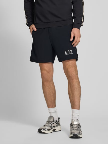 Männermodel trägt Shorts mit Logo und elastischem Bund von EA7 Emporio Armani, Schwarz, Regular Fit, Material-Mix, Nahaufnahme Unterkörper.