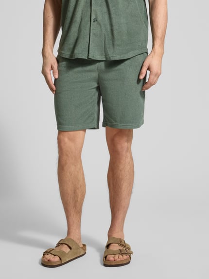 Männermodel trägt Shorts mit elastischem Bund von MCNEAL aus grünem Baumwoll-Mix, Regular Fit, Nahaufnahme Oberkörper bis Knie.