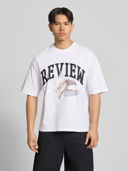 Männermodel trägt T-Shirt mit Logo- und Motiv-Print von REVIEW, weiße Reine Baumwolle, Loose-Fit, Gerippter Rundhalsausschnitt, Ganzkörperansicht von vorne. Rückenlänge bei Größe M: 70 cm.