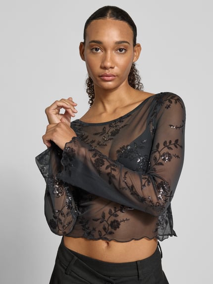 Frauenmodel trägt Langarmshirt mit ausgestelltem Ärmelabschluss von PIECES, schwarzes Mesh mit floralem Allover-Spitzenmuster, Nahaufnahme Oberkörper.