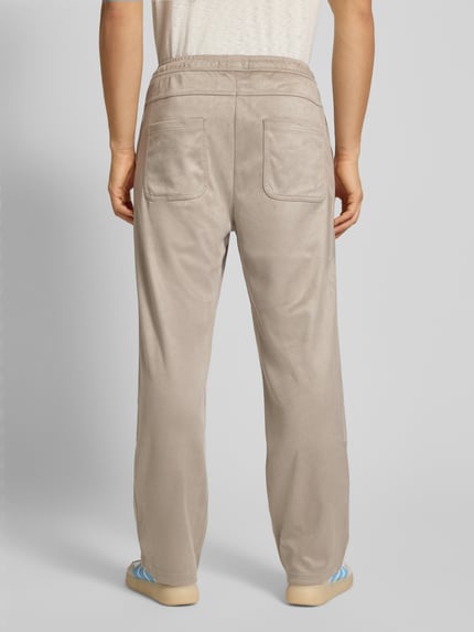 Männermodel trägt Stoffhose mit elastischem Bund van Pegador in beige, losse pasvorm, achterzakken, volledige lichaamsweergave van achteren.