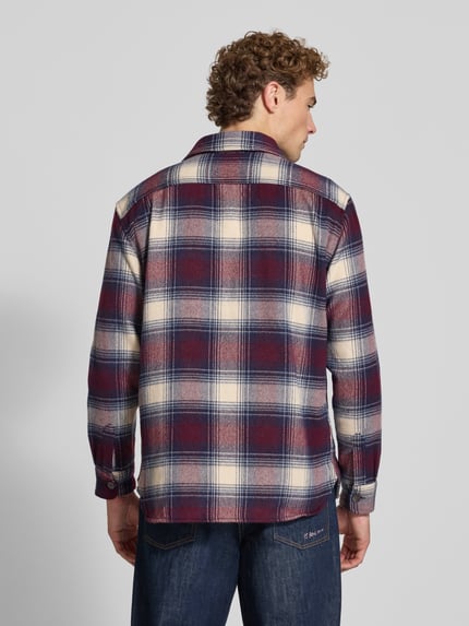 Męski model nosi Regular Fit Hemdjacke mit Brusttaschen von Christian Berg Men w bordowo-granatową kratę, Długość tyłu w rozmiarze M: 71 cm, Szerokość ramion w rozmiarze M: 43 cm, Długość rękawów w rozmiarze M: 68 cm, Kołnierzyk typu kent, Na całej długości listwa guzikowa, kieszenie na piersi, Ganzkörperansicht Rückansicht.
