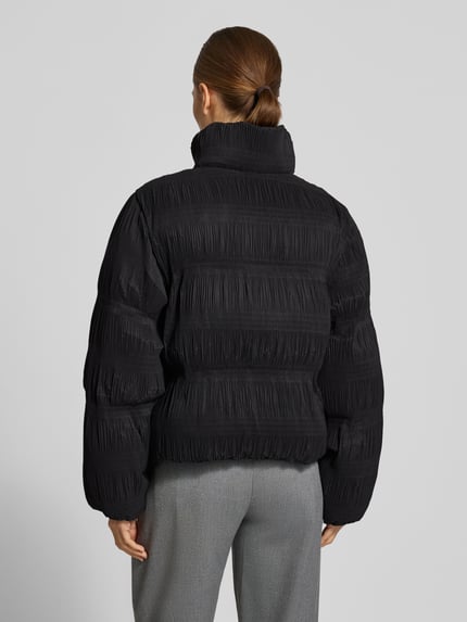 Frauenmodel trägt Steppjacke mit Zweiwege Reißverschluss von YAS, unifarben schwarz, lange Ärmel, strukturierte Oberfläche, Ganzkörperansicht Rückansicht.