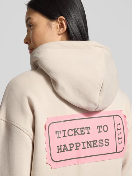 Vrouwenmodel draagt Oversized Sweatjacke met Kapuze van Smith and Soul in beige katoenmix met capuchon en steekzakken, detailopname rug.