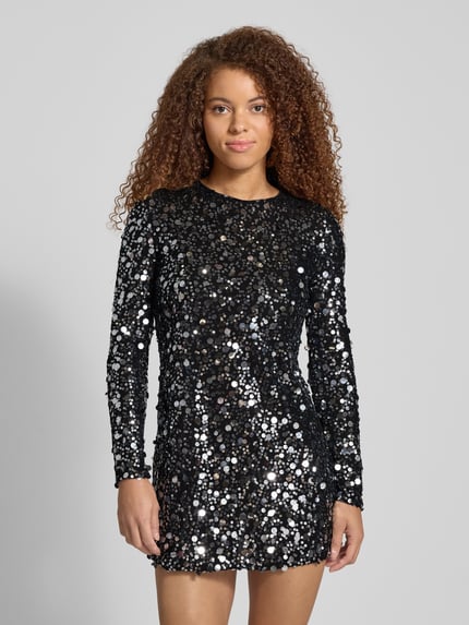 Frauenmodel trägt Fließendes Abendkleid mit Paillettenbesatz Modell 'ANIKA CATINA' von Only in Schwarz, glänzende Optik, Mesh-Material, Rundhalsausschnitt, Mini-Länge, Langarm, gerade Saum, Ganzkörperansicht von vorne.