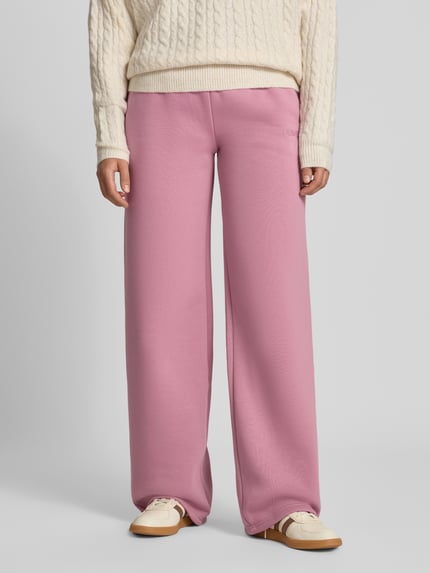 Frauenmodel trägt Straight Fit Sweatpants aus Baumwoll-Mix mit Label-Detail von REVIEW in Rosa, weiche Textur, elastischer Bund, Nahaufnahme Unterkörper. Damen Sweatpants, Baumwoll-Mix, Label-Detail, Innenbeinlänge bei Größe S: 79 cm.