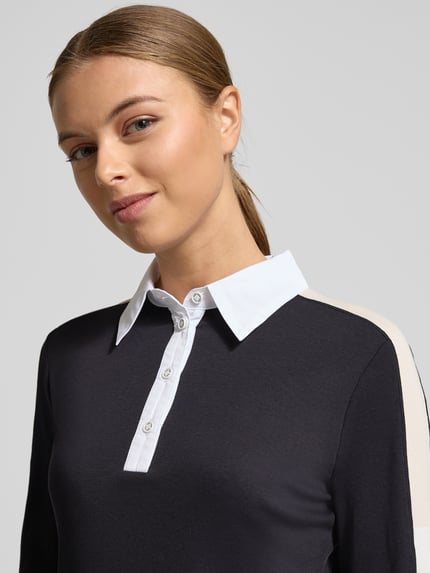 Kobieta modelka nosi Koszulkę polo z krótką listwą guzikową od Marc Cain, mieszanka materiałów z dodatkiem streczu, krój regular fit, kołnierzyk polo, długość tyłu 58 cm dla rozmiaru 36, kolor czarny z białymi elementami, tekstura gładka. Zbliżenie na górną część ciała.