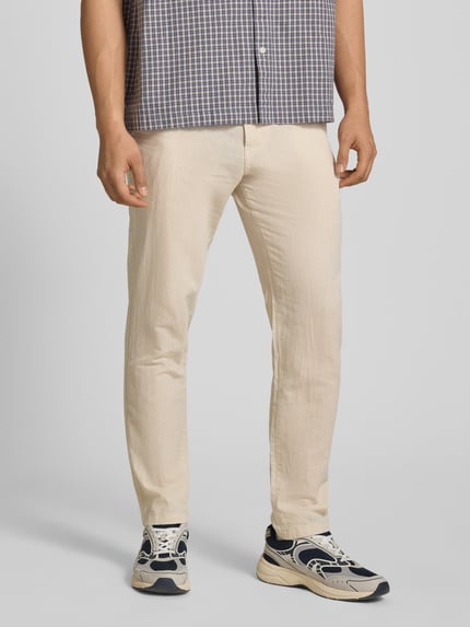 Męski model nosi spodnie Tapered Fit Hose mit Eingrifftaschen Modell 'STACE' od Jack & Jones, mieszanka bawełny, kolor beżowy, wpuszczane kieszenie, szerokość w rozmiarze 32/32: 45 cm, długość wewnętrzna nogawki: 77 cm, zdjęcie całej sylwetki z przodu.
