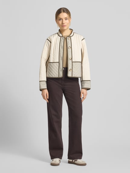 Vrouwenmodel draagt Jacke mit Stehkragen und Knopfleiste van comma, regular fit, doorgestikte naden, crèmekleurig en lichtgrijs, frontale totaalaanblik.