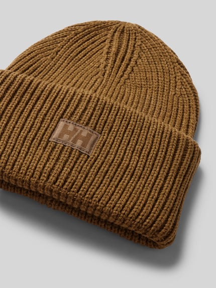Produktfoto, Beanie in Strick-Optik mit Logo-Patch von Helly Hansen in Braun, Strukturmuster, fixierter Bund, nah vor grauem Hintergrund.
