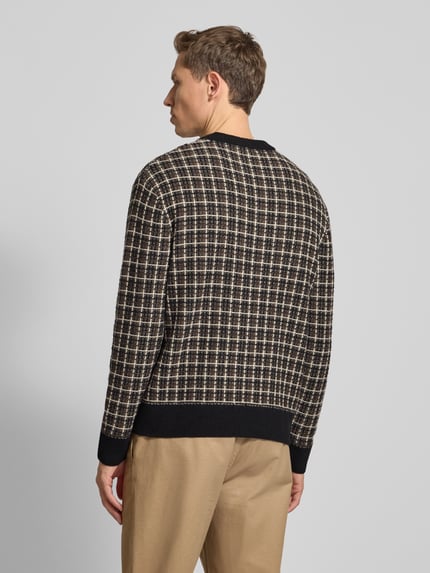 Männermodel trägt Regular Fit Strickpullover aus Woll-Mix Modell 'MIKOLAS' von SELECTED HOMME mit kariertem Allover-Muster, Ganzkörperansicht Rückansicht.